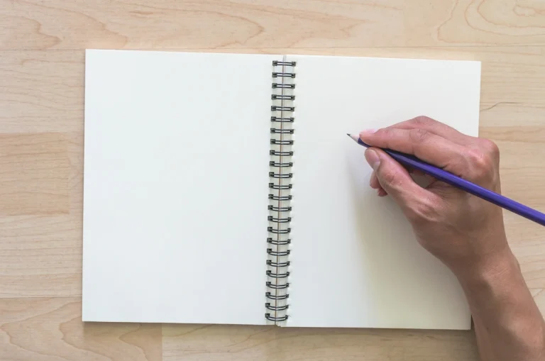 Une personne qui tient un stylo sur un carnet avec des pages blanches