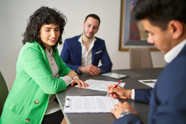Un homme qui signe un document devant une femme en costume verte et un autre homme