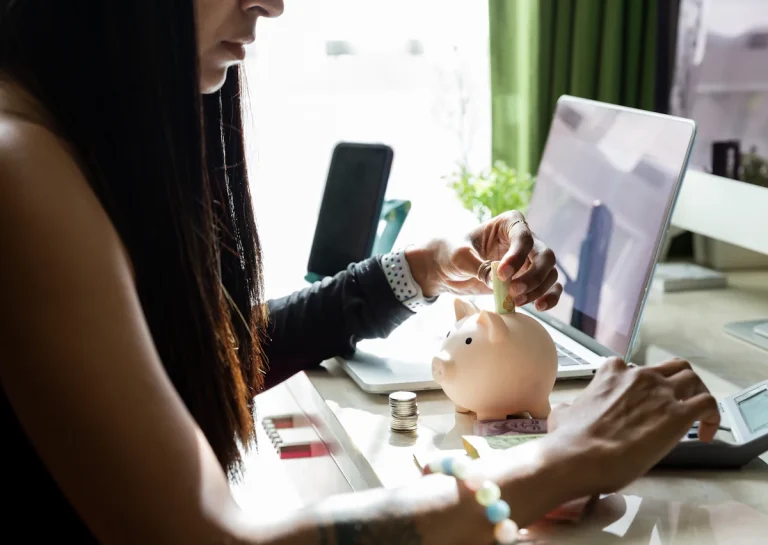 Une jeune femme qui met un billet dans une tirelire en faisant des calculs sur une caclulatrice