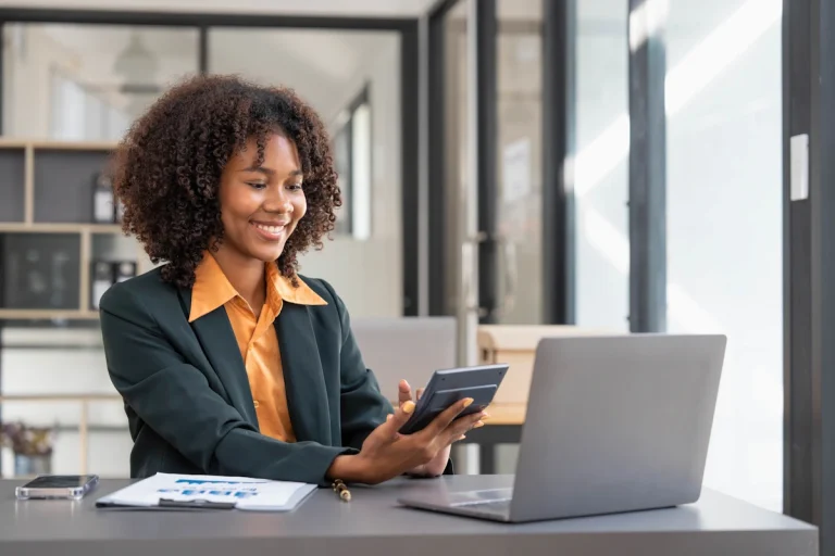 Une femme devant un ordinateur qui tient une calculatrice