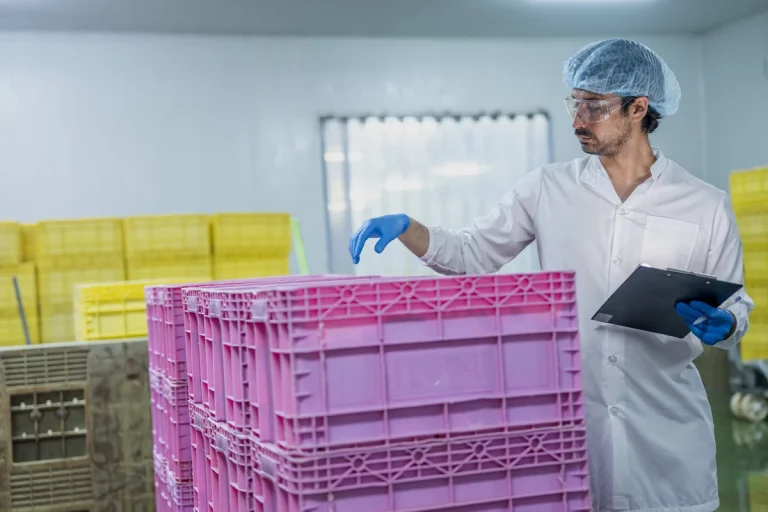 Un homme en blouse blanche et bonnet prêt d'une palette de stockage en plastique