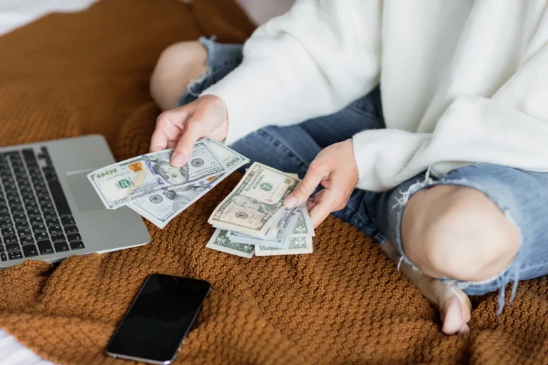 Une femme qui compte de l'argent assis sur le lit devant son ordinateur