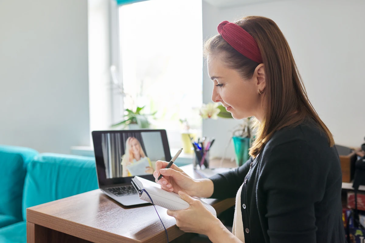 Une femme qui prend des notes devant une vidéo sur un ordinateur